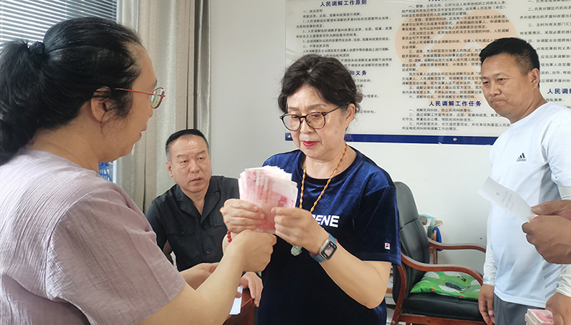 頭題片，5月30日，某藥業(yè)公司按協(xié)議約定完成第一期履行義務(wù)，將十萬現(xiàn)金交到法院，調(diào)解員付菊（左一）清點(diǎn)無誤之后交到農(nóng)民工委托代理人徐某手中