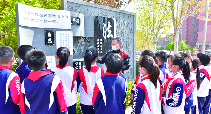 頭題圖，普法志愿者在憲法墻前給學生們普及法律知識。